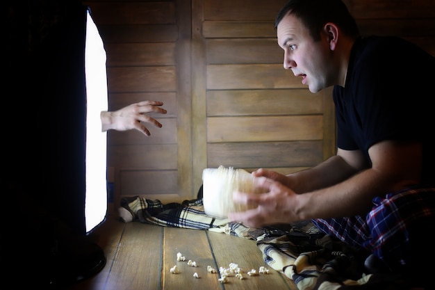 Young man watching television at home on the floor and eating popcorn