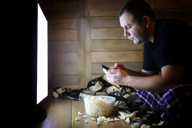 Young man watching television at home on the floor and eating popcorn