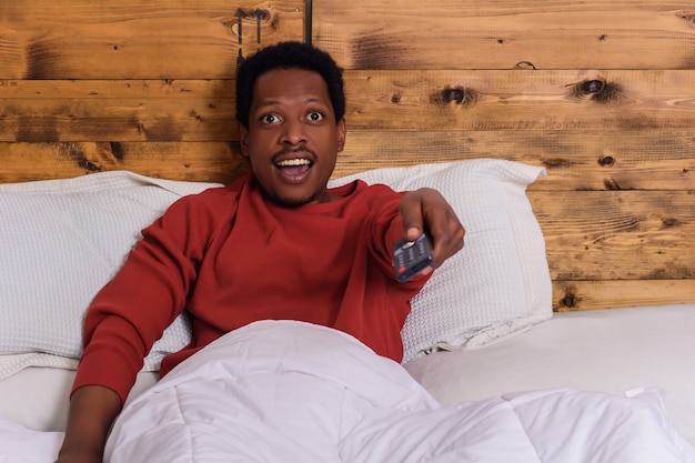 Photo young man watching tv on bed at home.