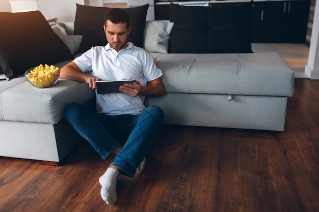 Young man watching tv in his own apartment. watching movie or program. sit on floor and use tablet.