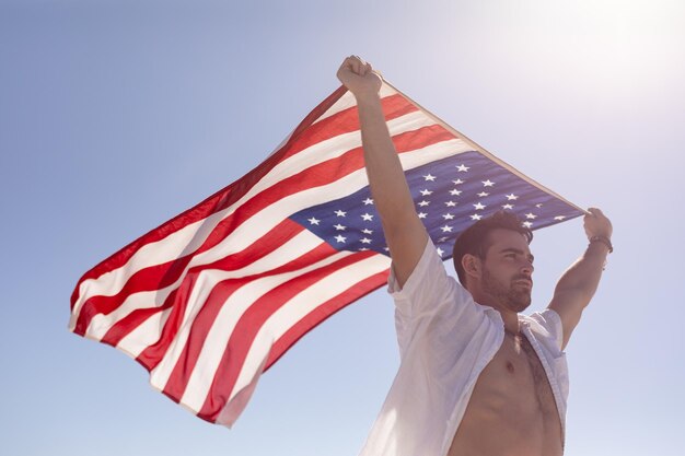 Young man waving american flag on beach in the sunshine