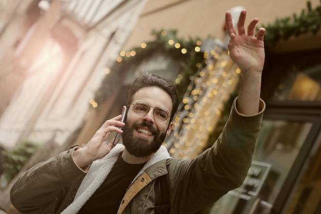 Young man waving on the street and talking on the phone