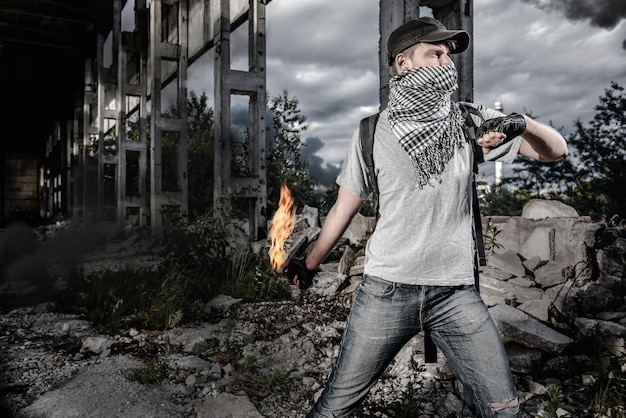 Young man wearig mask throwing bottle while fire under bridge