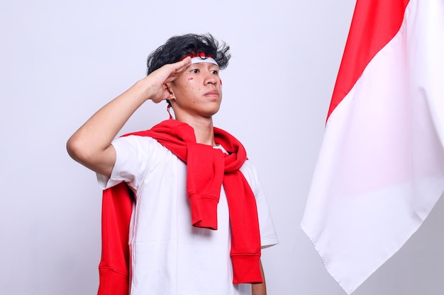 写真 インドネシア独立記念日のお祝いにインドネシア国旗に敬礼する白いシャツを着た若い男性