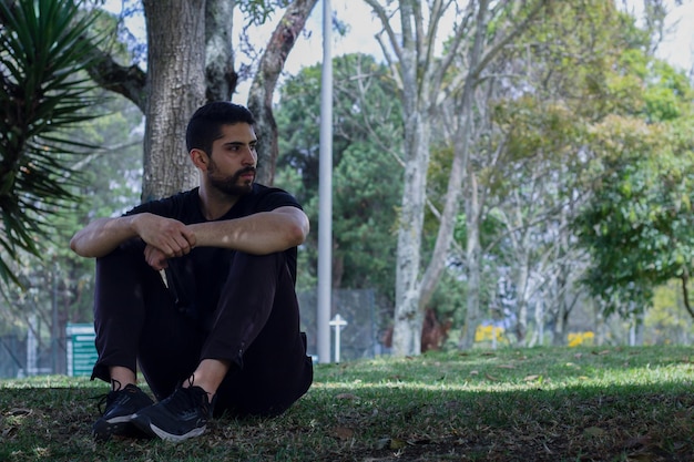 Photo young man wearing athletic wear sitting in the park exercising yoga