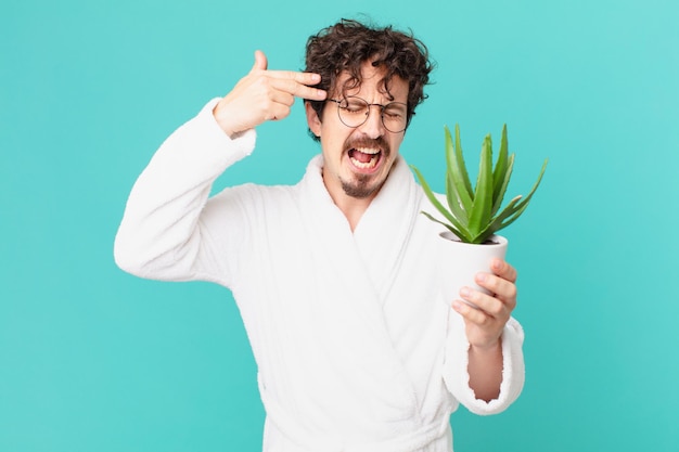 Young man wearing bathrobe looking unhappy and stressed, suicide gesture making gun sign