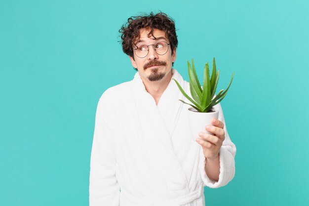 Young man wearing bathrobe shrugging, feeling confused and uncertain