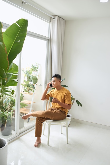 Young man wearing casual clothes talking on a mobile phone in the morning at a window