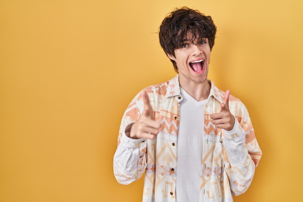 Young man wearing casual summer shirt pointing fingers to camera with happy and funny face. good energy and vibes.