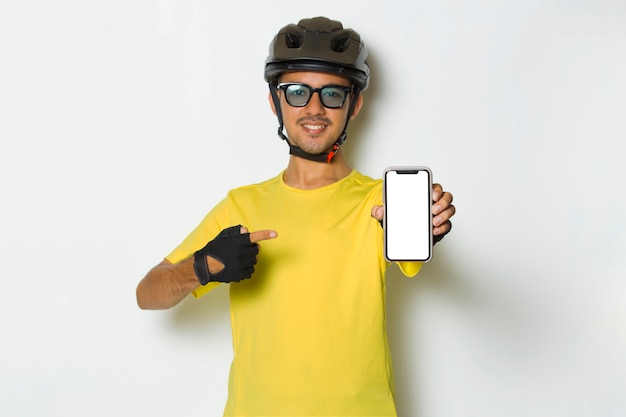 Young man wearing cyclist helmet hold mobile phone with blank empty screen on white background