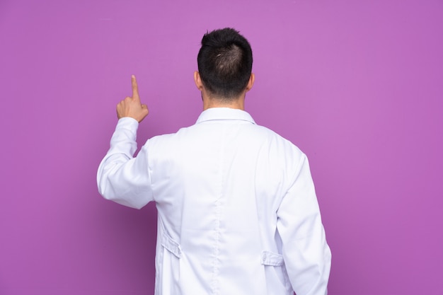 Young man wearing a doctor gown and pointing back