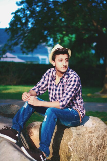 사진 공원 에서 바위 에 앉아 있는 동안 모자를 입은 젊은 남자