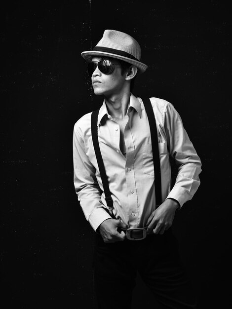 young man wearing hat standing against black background