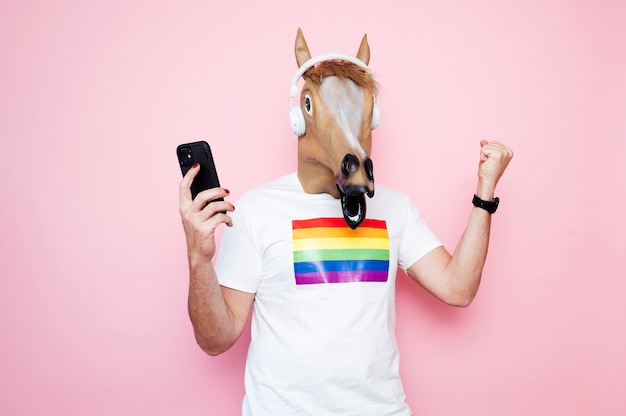 Young man wearing horse mask while using smartphone in studio with pink background