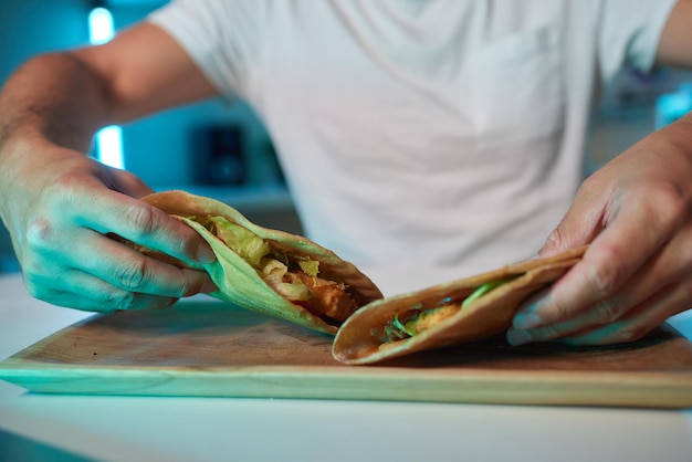 Foto un giovane con guanti di lattice che prepara un panino falafel in un pane pita con pomodoro e cipolla tritati