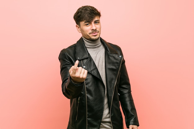 Young man wearing a leather jacket pointing with finger at you as if inviting come closer.