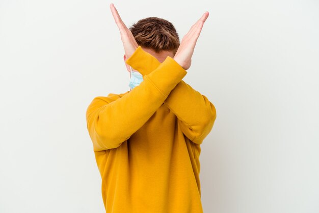 Photo young man wearing a mask for coronavirus isolated on white wall keeping two arms crossed