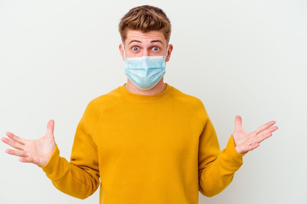 Young man wearing a mask for coronavirus on white celebrating a victory or success, he is surprised and shocked.