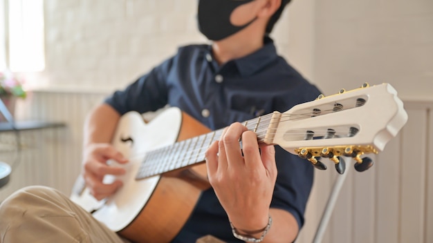 A young man wearing a mask playing guitar at home