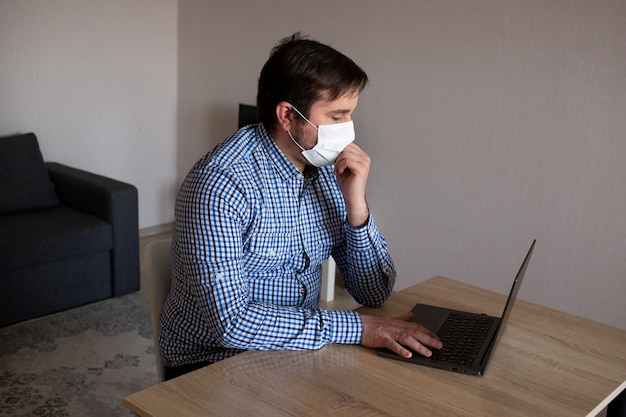 Young man wearing mask working on his computer from home, coronavirus, illness, infection, quarantine, medical mask