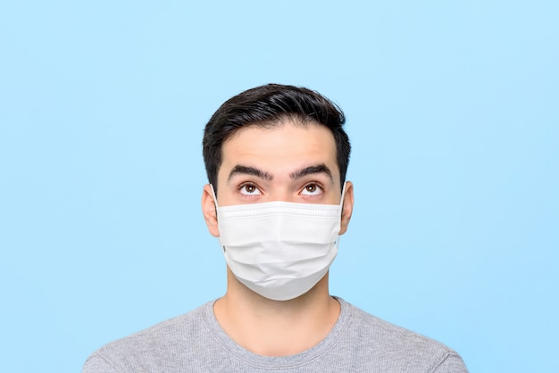 Young man wearing medical face mask thinking and looking up to empty space above isolated