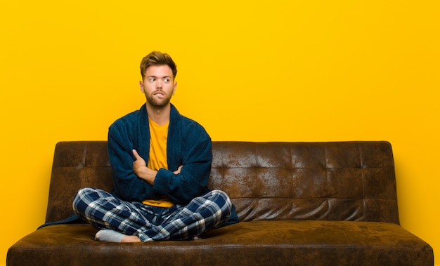 Young man wearing pajamas doubting or thinking, biting lip and feeling insecure and nervous, looking to copy space on the side 