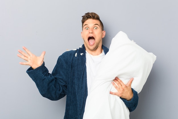 Young man wearing pijama holding a pillow celebrating a victory or success