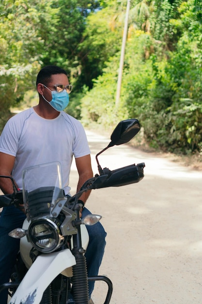 Young man wearing a protective mask and sunglasses riding a motorcycle on a country road