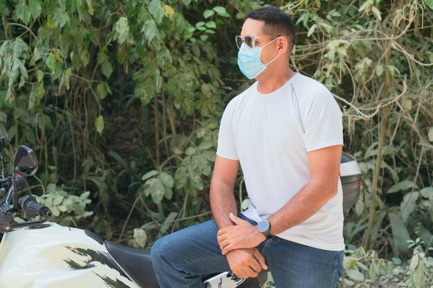 Young man wearing a protective mask and sunglasses riding a motorcycle on a country road