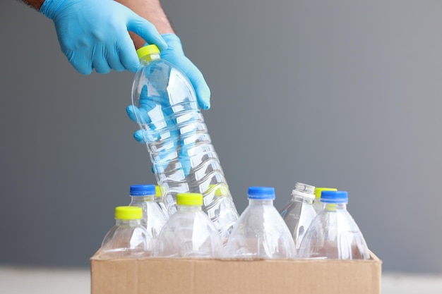 Un giovane uomo che indossa guanti di gomma ha sistemato le bottiglie di plastica in una scatola. presume che le bottiglie di plastica saranno una sorta di spazzatura prima di gettarle nel cestino.