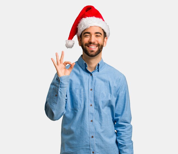 Young man wearing santa hat cheerful and confident doing ok gesture