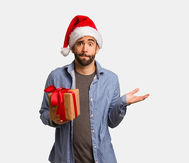 Young man wearing santa hat confused and doubtful
