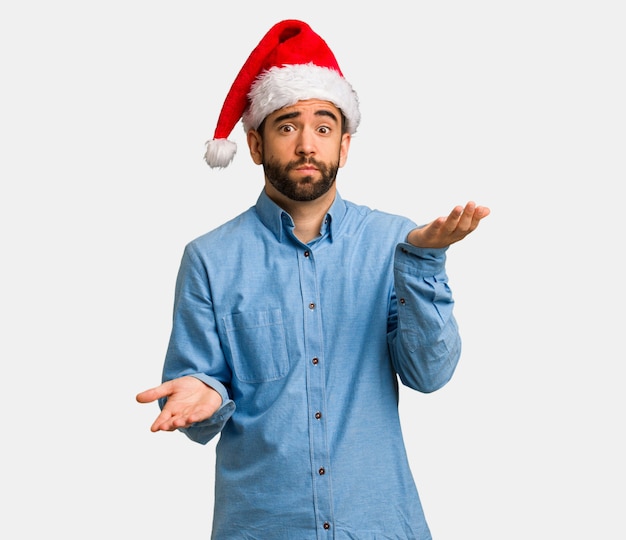 Young man wearing santa hat confused and doubtful