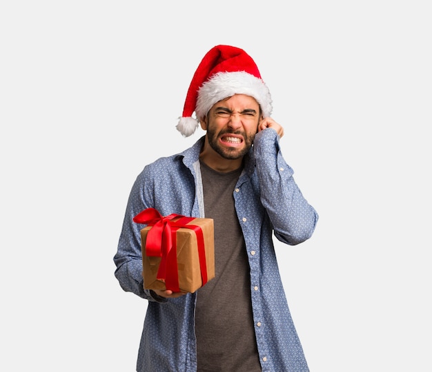 Young man wearing santa hat covering ears with hands