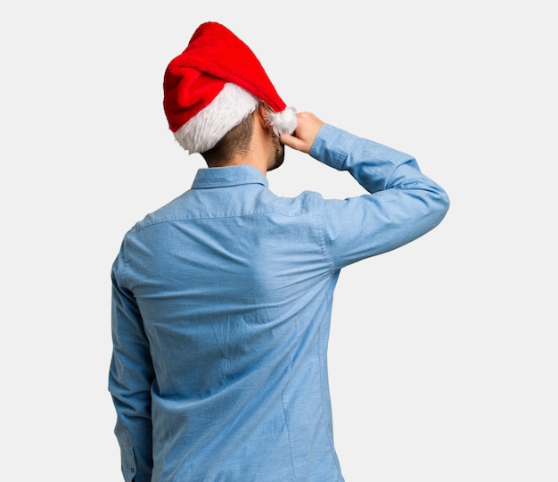 Young man wearing santa hat from behind thinking about something