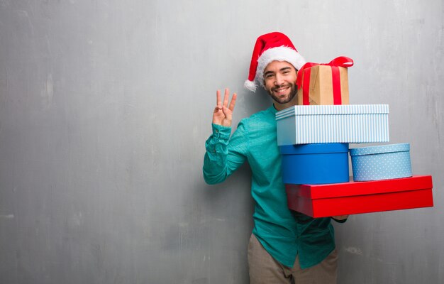 Young man wearing a santa hat holding gifts showing number three