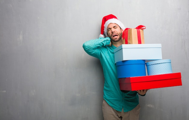 Young man wearing a santa hat holding gifts suffering neck pain