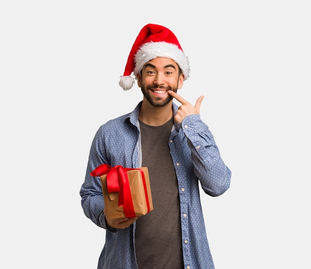 Young man wearing santa hat smiles, pointing mouth