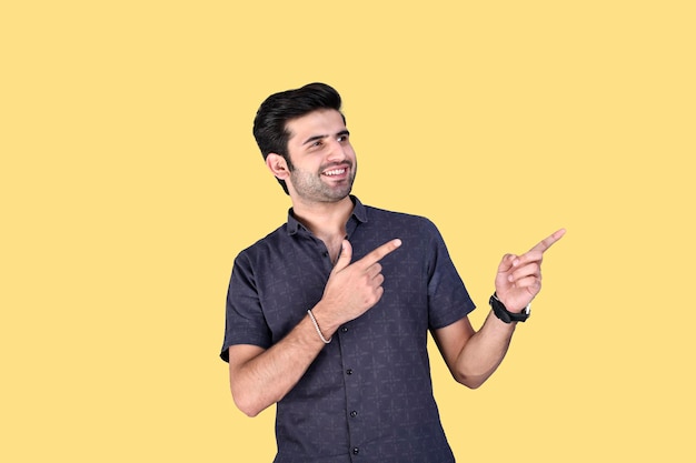 Молодой человек в летней одежде указывает в сторону с улыбкой, показывая что-то индийско-пакистанскую модель