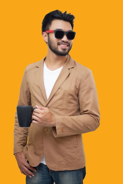 Young man wearing sunglasses holding coffee cup while standing against yellow background