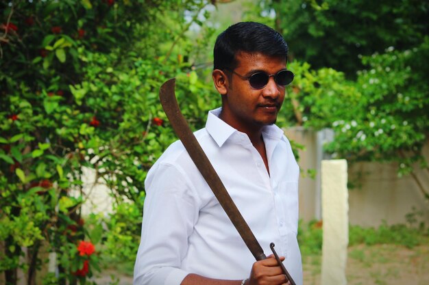 Young man wearing sunglasses holding knife against plants