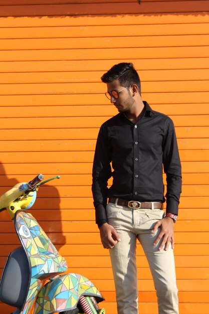 Young man wearing sunglasses standing against orange wall