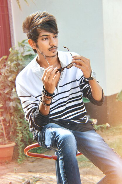 Photo young man wearing sunglasses while sitting on equipment in playground