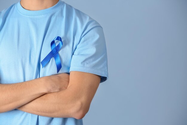 Young man wearing tshirt with blue ribbon on color background closeup Prostate cancer awareness concept