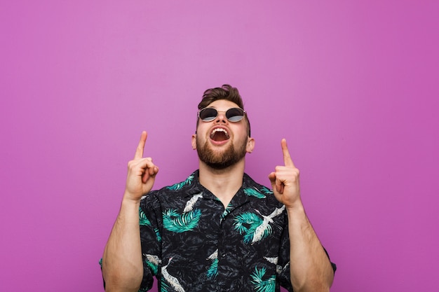 Young man wearing a vacation look pointing upside with opened mouth