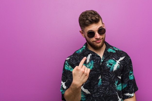 Young man wearing a vacation look pointing with finger at you as if inviting come closer