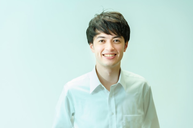 A young man wearing a white shirt and smiling in front of a white background