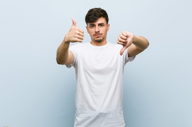 Молодой человек в белой футболке показывает палец вверх и вниз