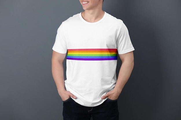 Young man wearing white tshirt with image of LGBT pride flag on grey background