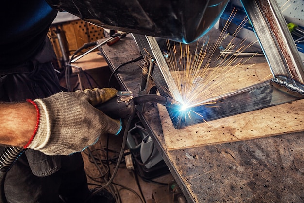 A young man welder  in a welding mask and construction gloves,  weld a metal welding machine